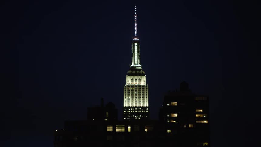 A building in a city with the architecture of a tower and at the top of it there are many lights and it is night