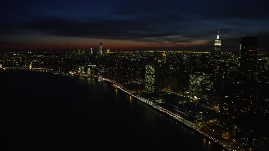 A city is shown lit up at night next to a lake via aerial view