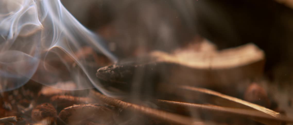 A smoke slowly wafts upwards from smoldering piece of wood