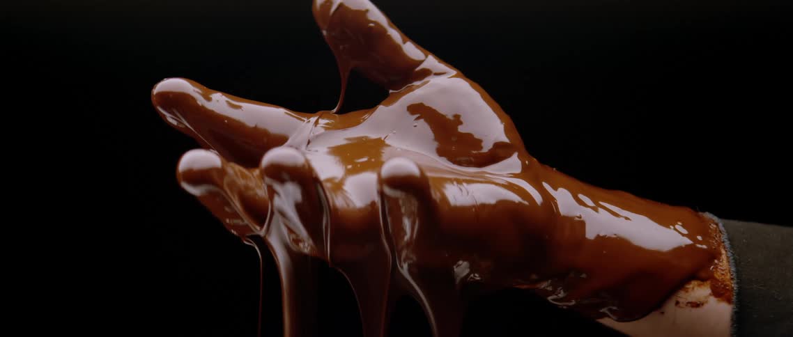 A persons hand covered in chocolate as it slowly drips down