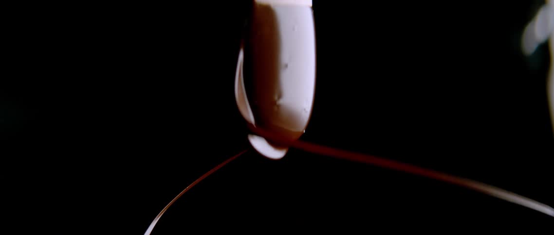 Chocolate syrup falling from rotating spoon moves through air in dark area