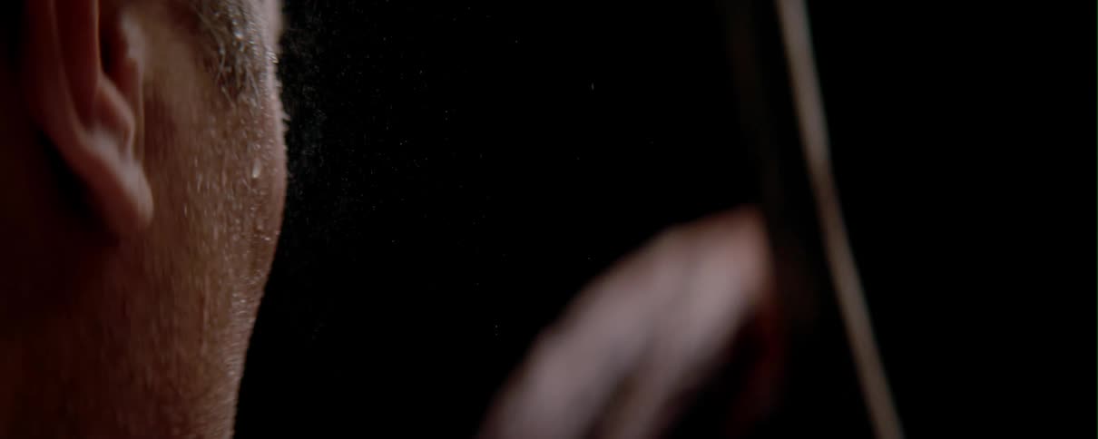 A man holds a violin stick in a dark room