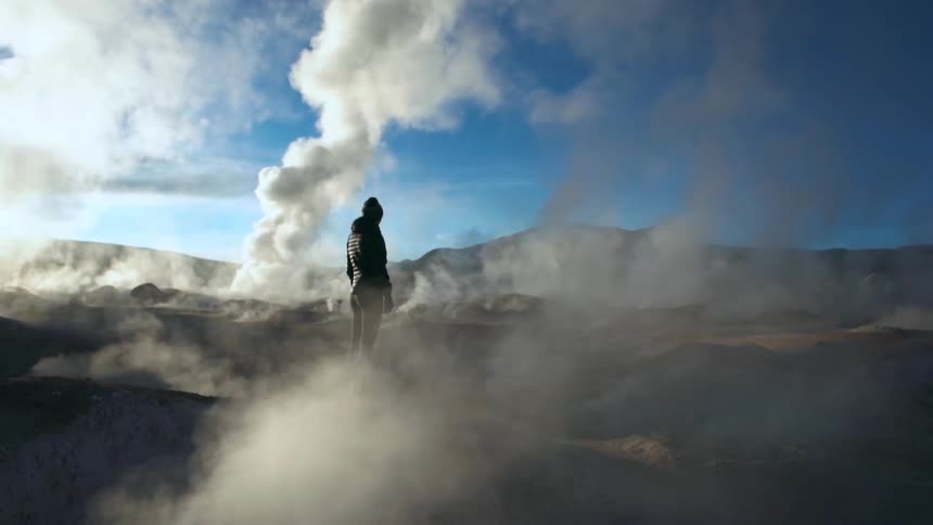 A person wearing hoodie standing in a lava mountain bringing smokes from the ground