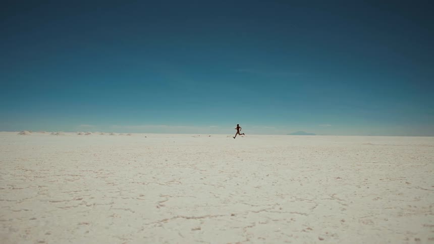 Person running across a vast flat salt flat under a clear blue sky
