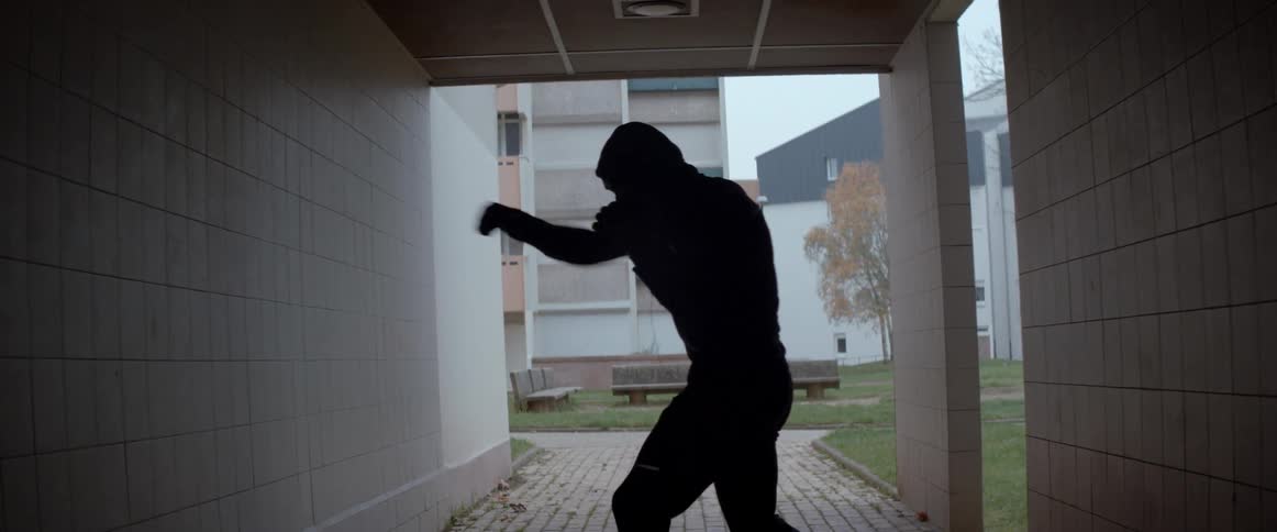 A man shadow boxes and throws numerous punches near a building