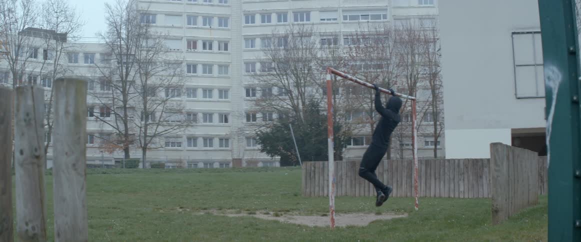 A man doing pull ups using a goal bar in a football field