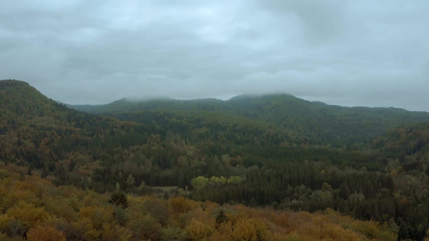 Forested mountains with trees in fall colors under a cloudy sky