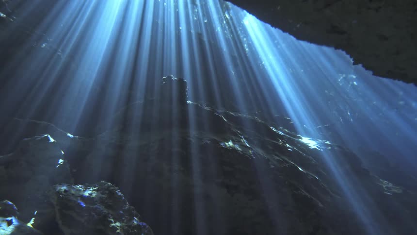 Sunlight shines through the clear water inside an underwater cave