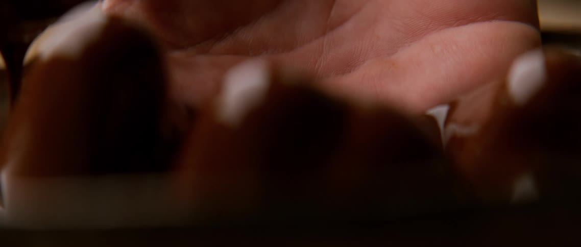 Extreme closeup of a hand being lifted from a bowl covered in liquid chocolate