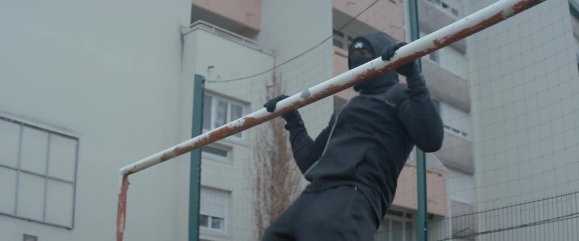 A male adult doing pull ups from a goal post while wearing mask and hoodie