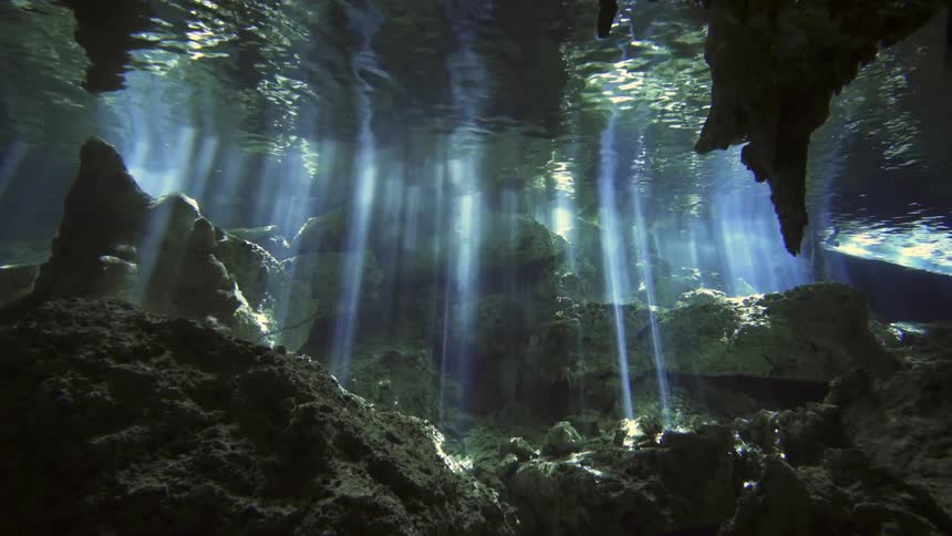 Sunlight shines through the clear water inside an underwater cave