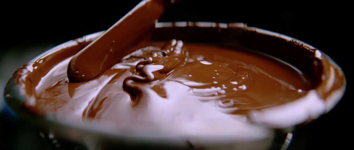 Spatula being dipped into a container with melted chocolate