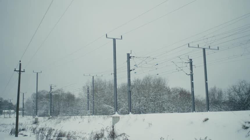 Utility poles line the railroad tracks standing tall against the backdrop of falling snow