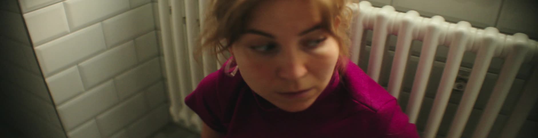 Woman with hoop earrings brown hair and red top leans against the column heater and looks around