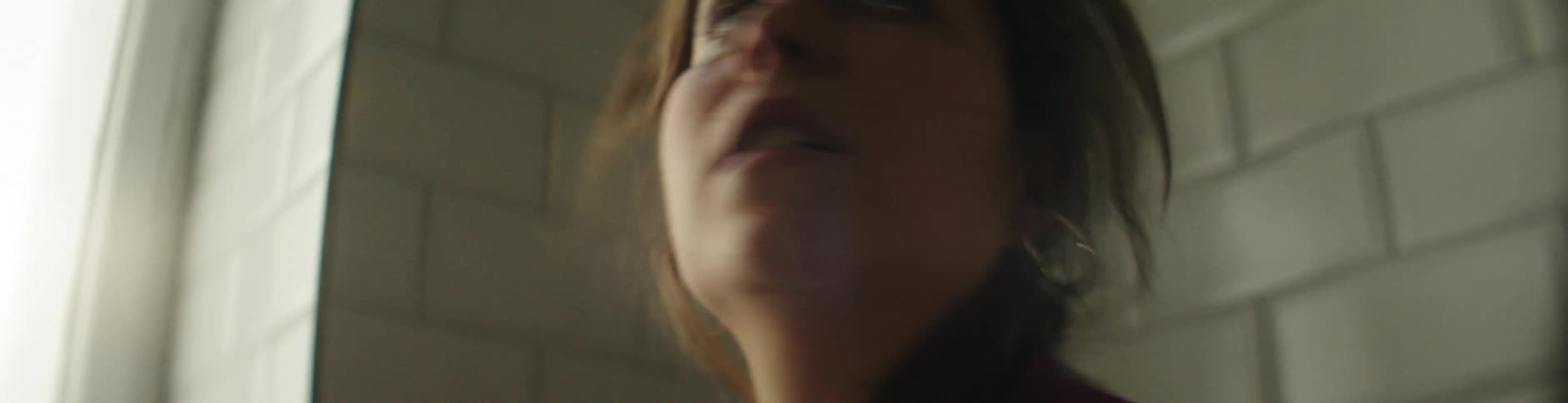 A woman lifts her head and looks out the window and towards the door fearfully as if she heard something