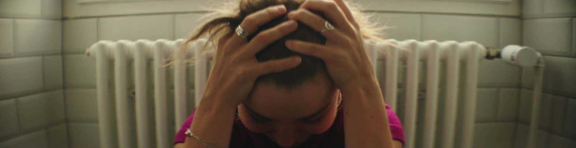 A woman sitting with her back to the window is running her hands through her hair as she is looking down