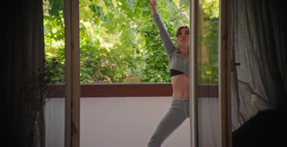 A young woman in grey outfit is doing yoga on the terrace on a sunny summer day