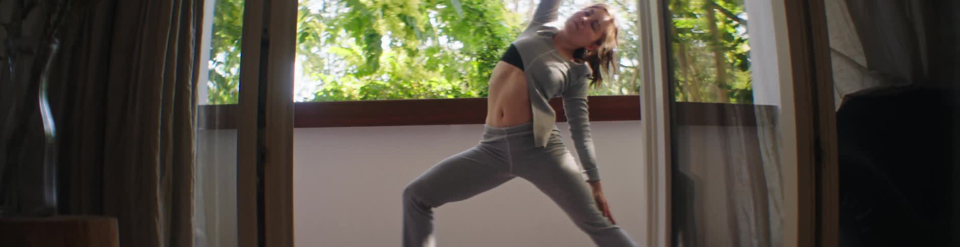A woman in a gray top and leggings doing exercises on the balcony