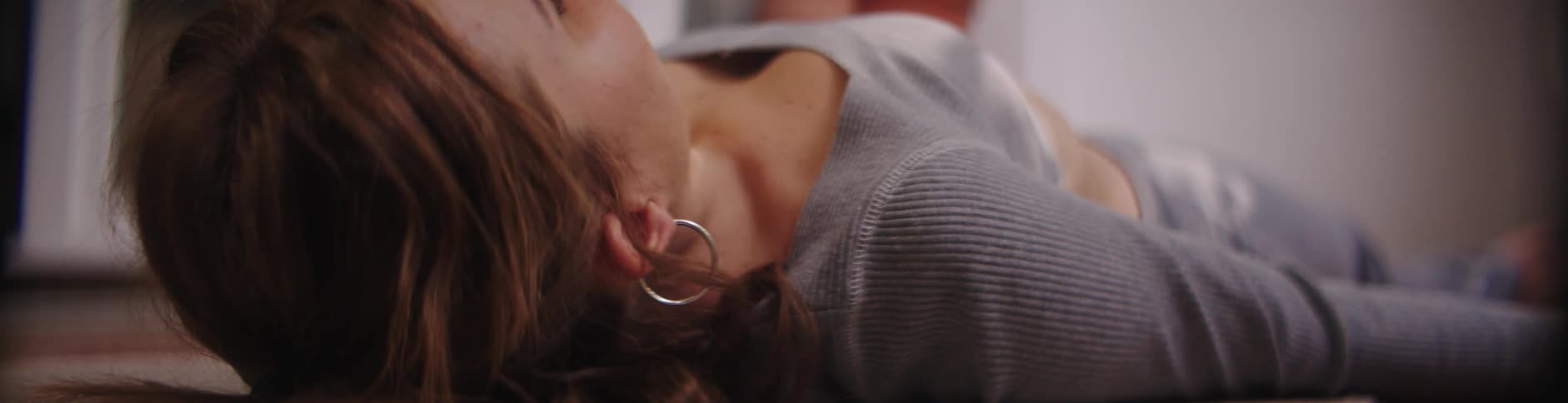Woman with brown hair hoop earrings gray shirt and leggings lies on the floor breathing