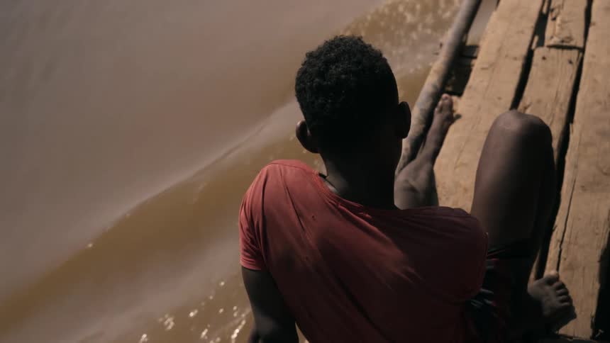 A man sitting on a wooden boat while floating on a muddy river