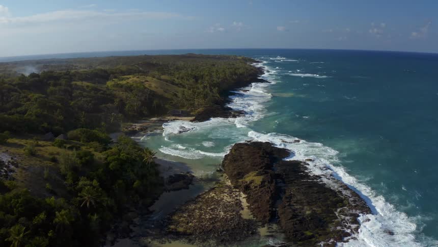 Waves flow onto coast of long forested peninusla on a cloudy day