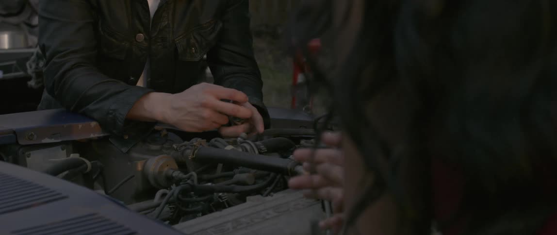 A man and woman are standing over a car engine
