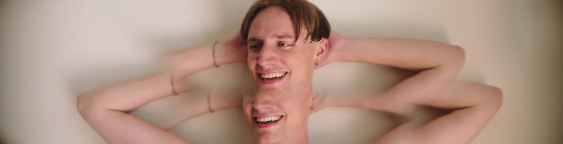 A joyful man with hands behind his head wearing a smile