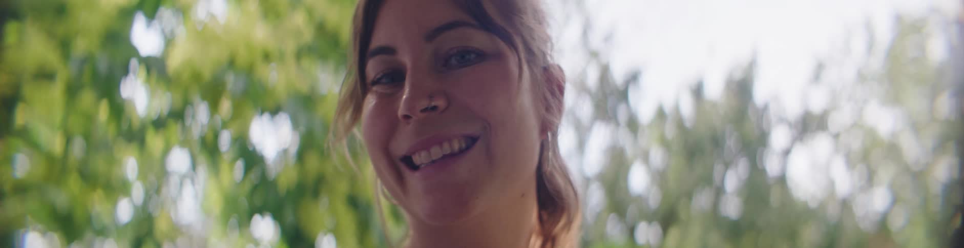 A woman standing outdoors looks up and smiles for the camera