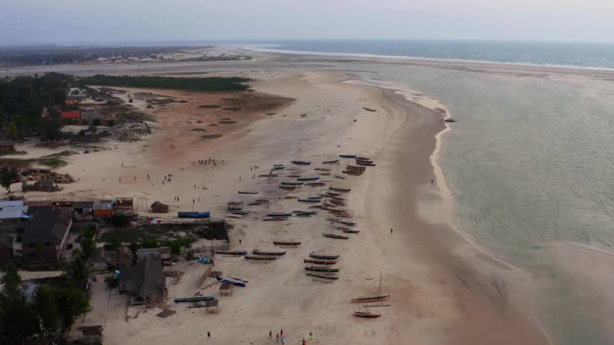 Aerial of canoes and people walking around the beach side at midday