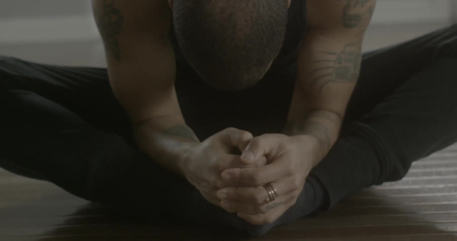 A man is sitting indian style on the floor leaning forward