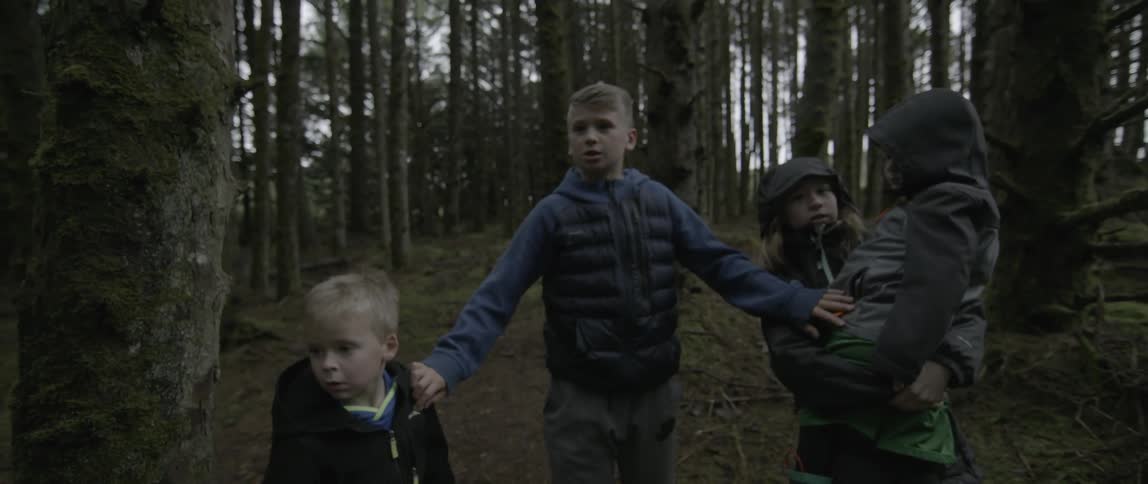 Children walking through the woods come to a stop at the direction of the elder child