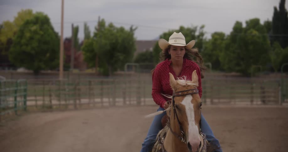 A blonde woman riding a horse on a ranch