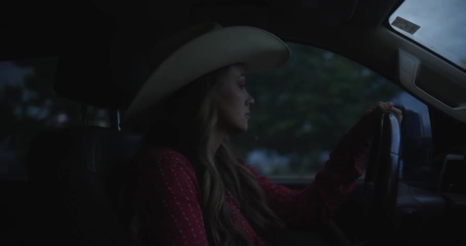 A woman wearing a cowboy hat driving a car at dusk