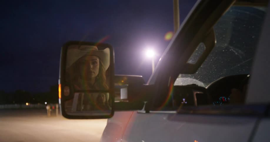 Lady on cowboy hat drives a car on the road at night