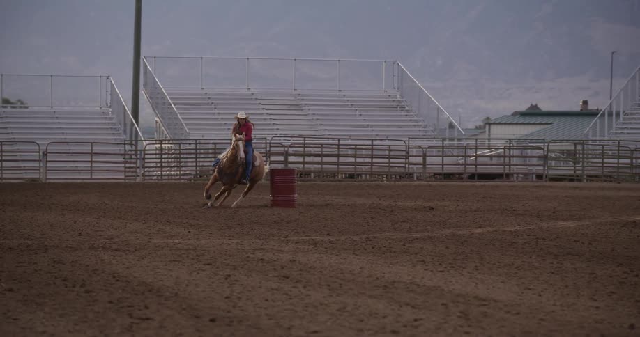 A woman wearing a cowboy hat training a horse as she ride round a barrel