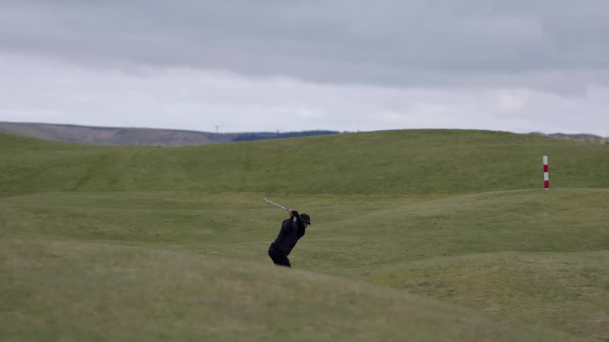 A male at the field swinging at a golf