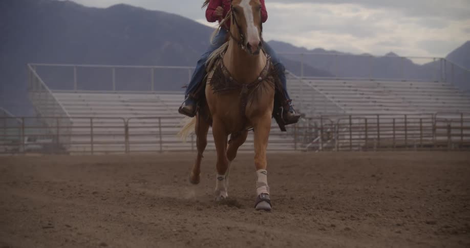 Woman on top of a horse riding in slow motion in a sandy field
