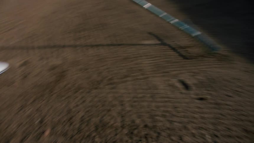 A person wearing white sneakers is raking some land and leaving the marks of the rake on the ground