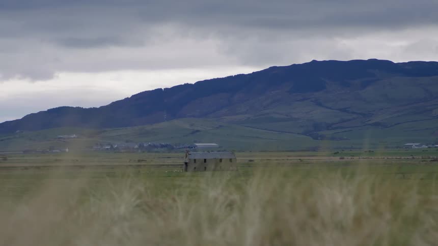 A building in a field with grasses and a mountain in the background