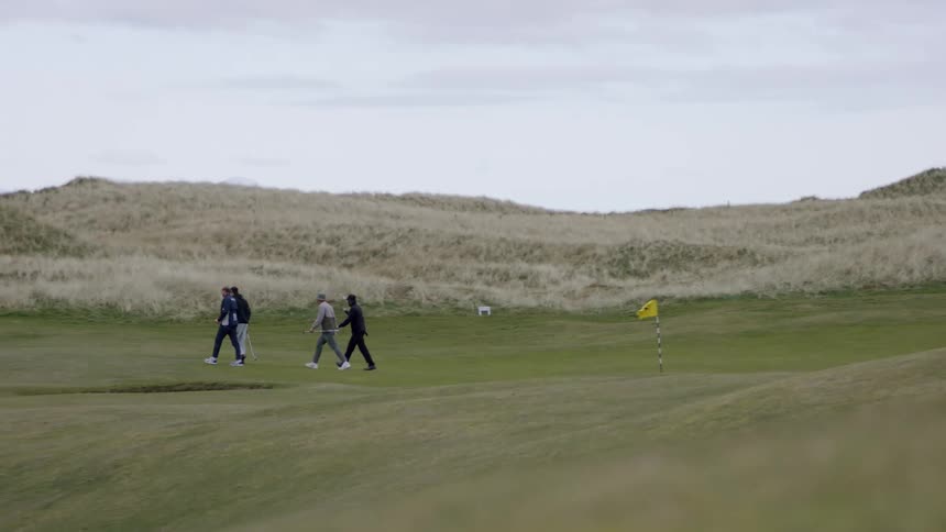 Four people are walking on a golf course on a cloudy day