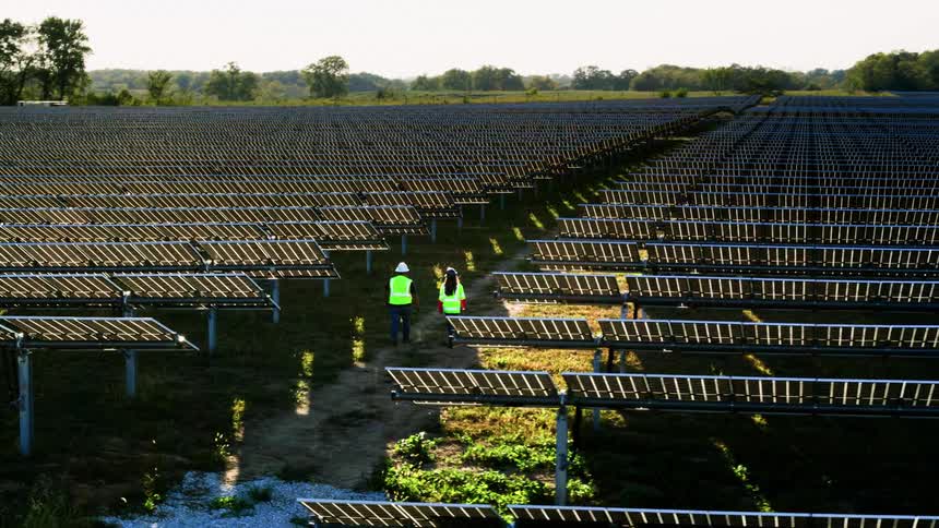 Two solar workers are walking between solar panel rows on a solar farm