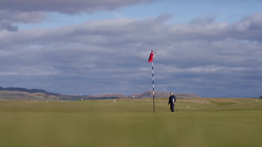 View of a golf course with a golfer swinging a club to hit a ball