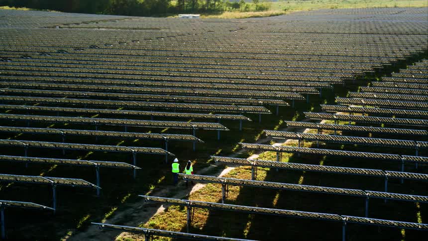 Two utility workers are walking between solar panels on a solar farm