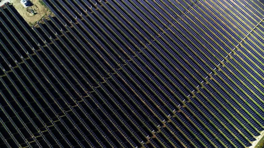 Eagle's eye view from above of a solar farm with sunlight reflecting off panels
