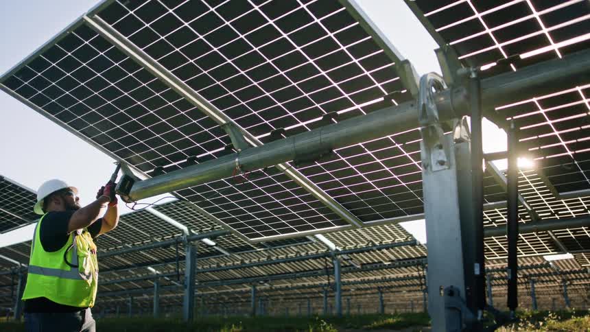A maintenance worker is using a drill on a solar panel