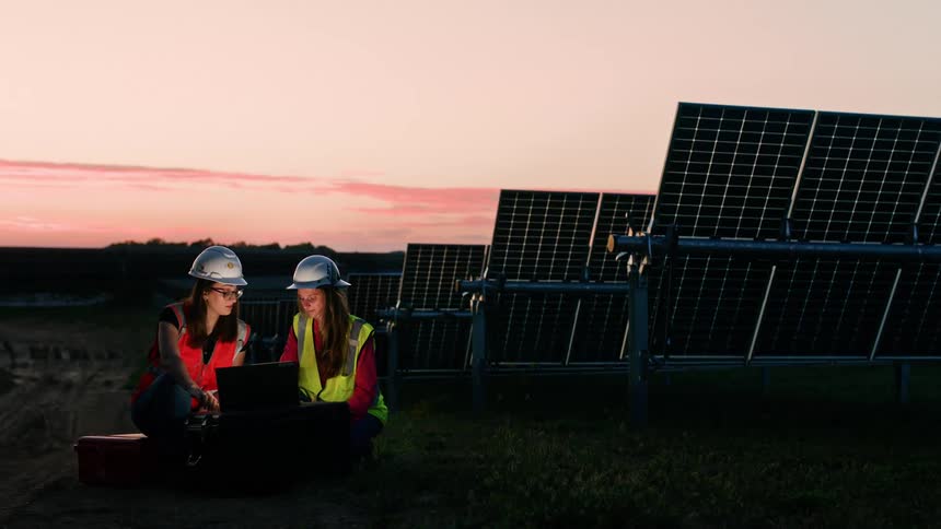 Two female engineers work late in the evening at sunset in solar field near panels