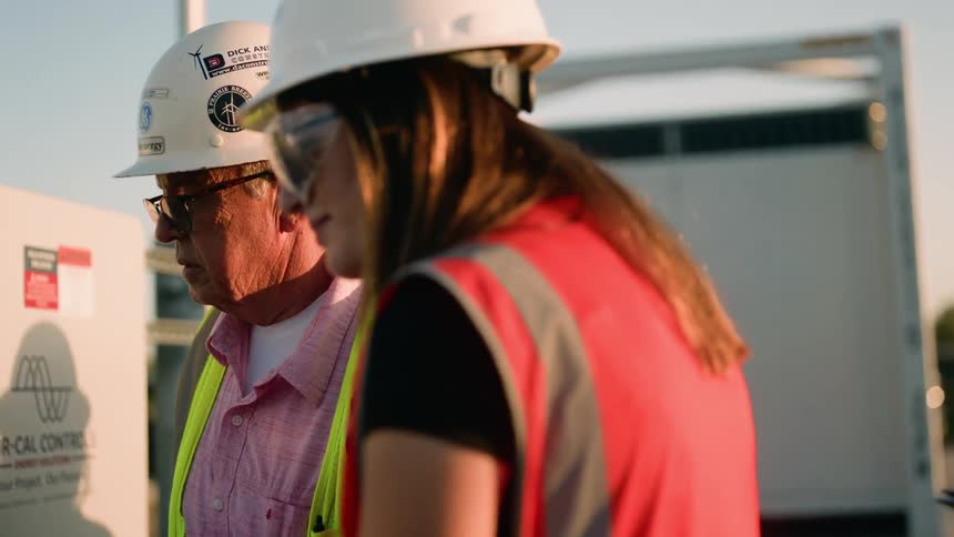 Minority utility workers looking into electrical box while wearing safety helmet and safety vests