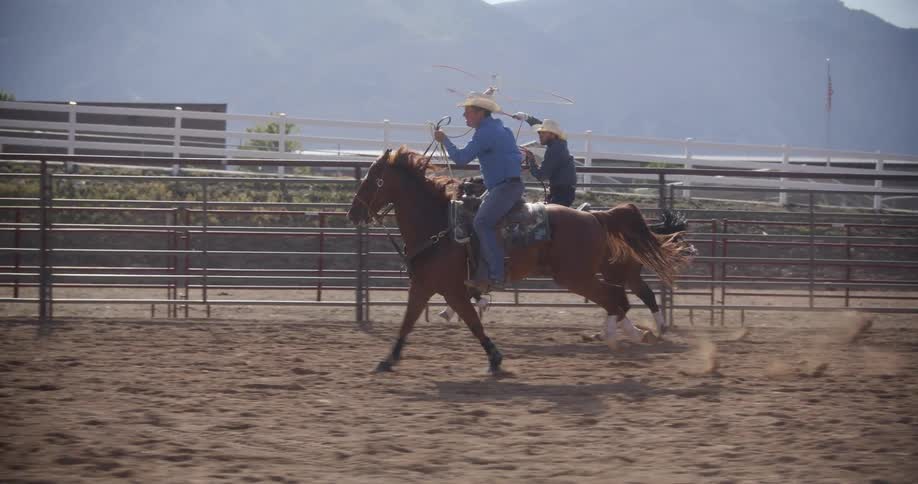 Two men riding horses and spinning ropes
