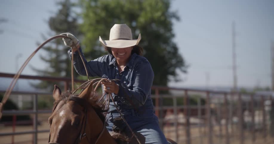 A woman riding on horseback smiles as she readies her lasso