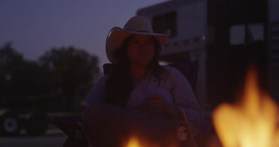 Cowgirl sitting near a campfire at night